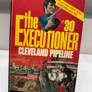 May include: Vintage paperback book titled "The Executioner: Cleveland Pipeline" by Don Pendleton. The cover features a man holding a gun, a cityscape, and a ship. The book is number 30 in a series.
