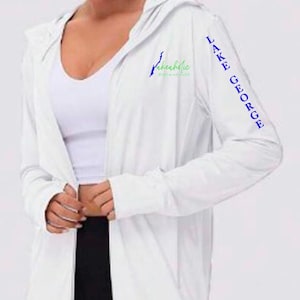 Puede incluir: Chaqueta blanca con cremallera con un logotipo azul y verde que dice "Lake George" en la manga derecha y "Lakeholic" en el lado izquierdo del pecho.