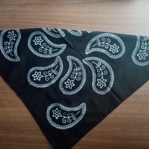 May include: Black bandana with a white paisley pattern. The bandana is folded into a triangle shape.