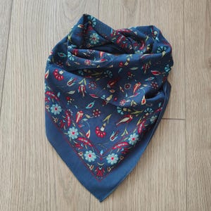 May include: A square scarf in a deep navy blue color featuring a repeating floral pattern in shades of red, light blue, and green. The design includes stylized flower motifs and thin stems arranged across the fabric with a decorative border.
