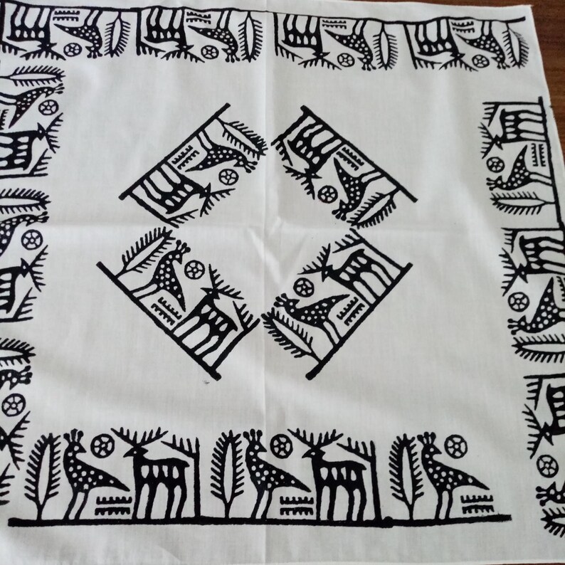 May include: White square textile with a repeating black pattern. The design features stylized deer, birds, and geometric shapes. The border has a repeating pattern of birds and other shapes. The center has four diamond-shaped designs.