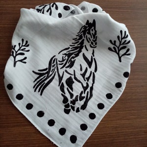 K&ouml;nnte beinhalten: Ein wei&szlig;es, dreieckiges Bandana mit einem schwarzen Siebdruckmotiv eines galoppierenden Pferdes in der Mitte. Der Stoff ist mit schwarzen Punkten entlang der unteren Kanten und stilisierten schwarzen Baumzweigmotiven an den Seiten verziert.