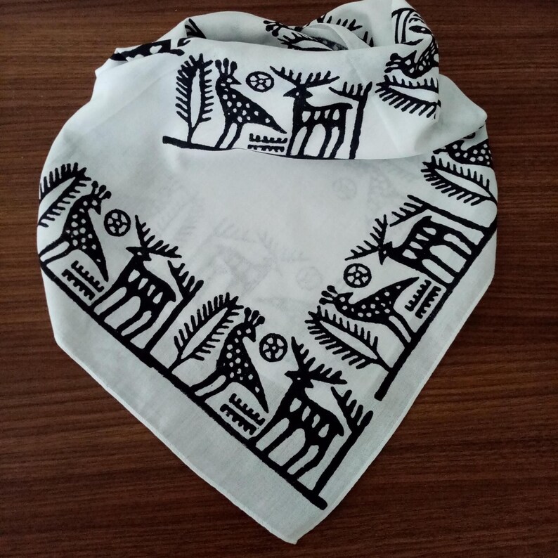 May include: White bandana with a black, stylized border design featuring deer, birds, and trees. The bandana is folded, showcasing the repeating pattern on the edges. The fabric appears to be cotton or a similar material.