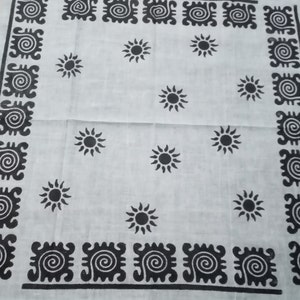 May include: White cloth with a repeating pattern of black suns and decorative black borders. The suns are evenly spaced across the fabric. The borders feature a repeating spiral design.