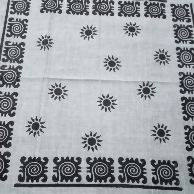 May include: White cloth with a repeating pattern of black suns and decorative black borders. The suns are evenly spaced across the fabric. The borders feature a repeating spiral design.