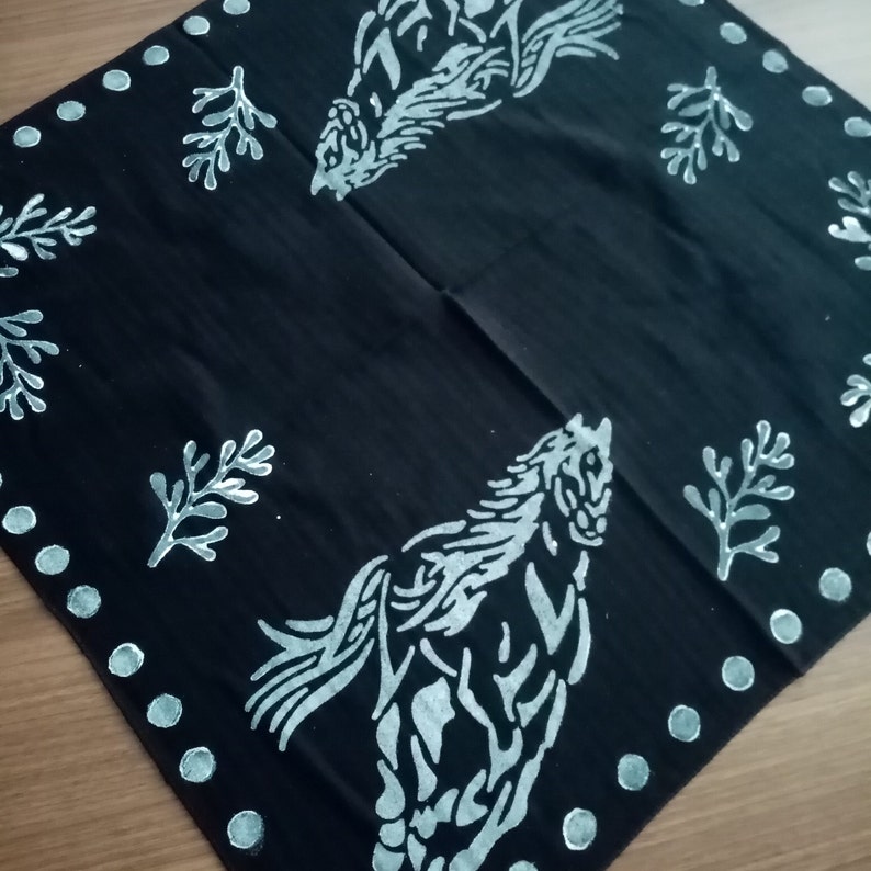 May include: Black bandana with a white horse design and white leaf patterns. The horse is running and has a flowing mane. The bandana has a white polka dot border.