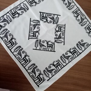 May include: White square cloth with a black geometric pattern. The design features stylized birds, deer, and abstract shapes. The border has a repeating pattern of birds and deer. The cloth is folded diagonally, showing the design in the center and along the edges.
