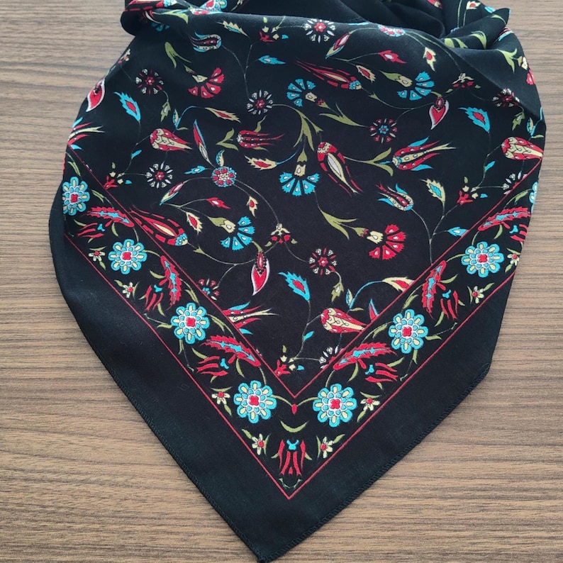 May include: A black square scarf featuring a vibrant floral pattern with red, turquoise, and green botanical motifs. The design includes a distinct border of repeating blue flowers and red tulip-like shapes, set against a solid black background.