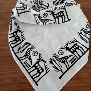 May include: White cotton bandana with a black and white print of stylized deer and trees around the border.