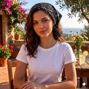 May include: A black bandana featuring a colorful floral and leaf pattern worn on the head, paired with a plain white short-sleeved t-shirt. The bandana is tied securely, showcasing vibrant red, blue, and green botanical motifs against a dark background.
