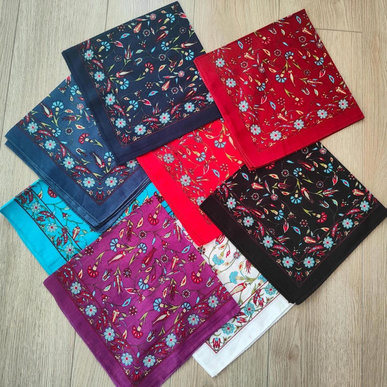 May include: A collection of seven square pocket squares or handkerchiefs arranged in a fan pattern. Each piece features a repeating floral pattern with red, blue, and white tulips and small blossoms, bordered by a solid colored edge in navy, red, black, purple, white, and turquoise.