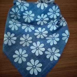 May include: A blue bandana with a white daisy pattern. The bandana is folded and knotted, showcasing the floral design. The fabric appears to be soft and lightweight, suitable for various uses.