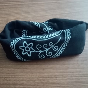 May include: A black bandana with a white paisley design. The bandana is folded and lying on a wooden surface.