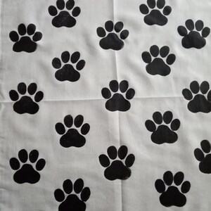 Pode incluir: Tecido branco com um padr&atilde;o repetitivo de pegadas pretas. As pegadas est&atilde;o uniformemente espa&ccedil;adas, criando um design l&uacute;dico e tem&aacute;tico de animais de estima&ccedil;&atilde;o. O tecido parece ser de algod&atilde;o ou material semelhante.
