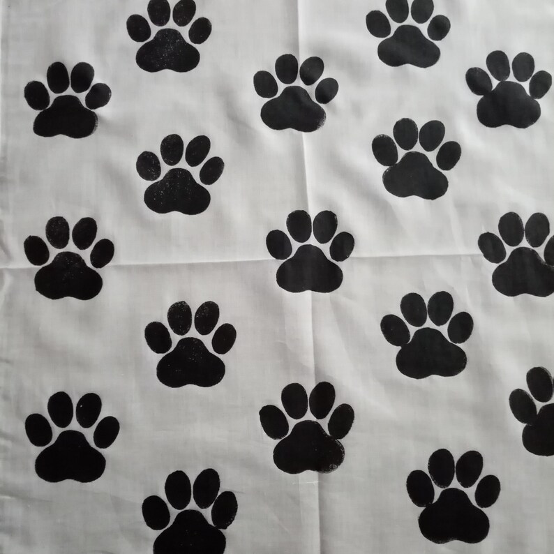 Pode incluir: Tecido branco com um padr&atilde;o repetitivo de pegadas pretas. As pegadas est&atilde;o uniformemente espa&ccedil;adas, criando um design l&uacute;dico e tem&aacute;tico de animais de estima&ccedil;&atilde;o. O tecido parece ser de algod&atilde;o ou material semelhante.