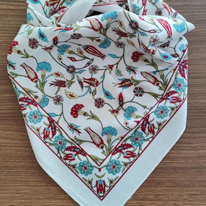 May include: A white square scarf featuring a repeating floral pattern with red tulips, blue carnations, and green stems. The design includes a decorative border with a geometric arrangement of flowers, creating a symmetrical and detailed botanical print.