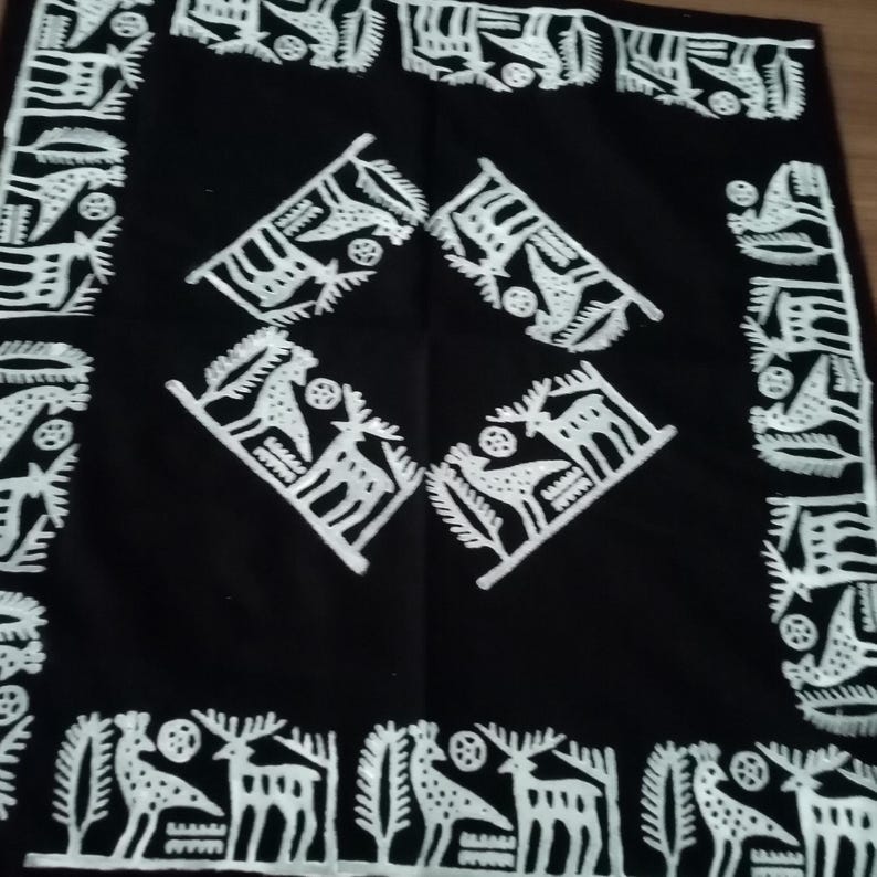 May include: Black square textile with white embroidered folk art designs. The border features stylized deer and trees. The center has four diamond-shaped designs with deer and bird motifs. A decorative piece.