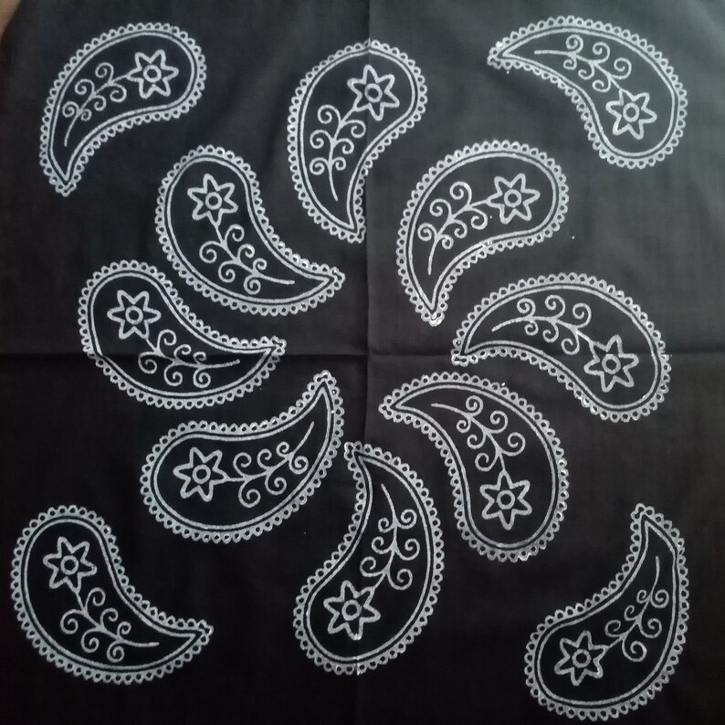 May include: Black fabric with a white paisley pattern. The paisley designs are arranged in a circular pattern.
