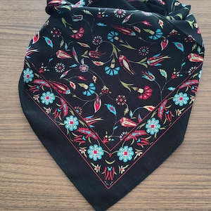 May include: A black square scarf featuring a repeating floral pattern with stylized tulips and blossoms in vibrant shades of turquoise, red, and white. The design includes a distinct border of flowers and leaves framing the central motif.