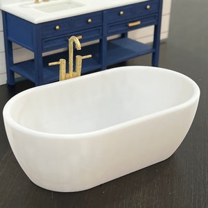May include: White oval bathtub with gold faucet fixtures. The bathtub is sitting on a dark wood surface.