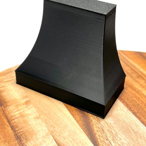 Pu&ograve; includere: Oggetto nero stampato in 3D con una superficie superiore testurizzata. L'oggetto ha la forma di una piramide tronca con una base larga e una cima stretta.