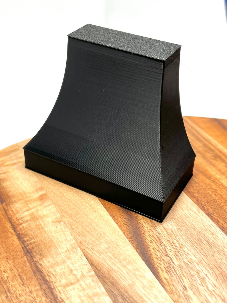 Pu&ograve; includere: Oggetto nero stampato in 3D con una superficie superiore testurizzata. L'oggetto ha la forma di una piramide tronca con una base larga e una cima stretta.