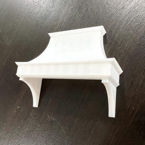 May include: White painted wooden kitchen range hood with a curved top and decorative trim. The hood has two brackets on the sides.