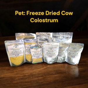 May include: Several silver resealable pouches of freeze-dried cow colostrum powder for pets. The pouches are labelled "Farm Organic" and feature a variety of images of farm animals and plants.