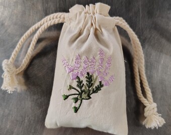 May include: A small, off-white drawstring bag with a floral embroidery design. The embroidery features a cluster of purple flowers with green leaves.