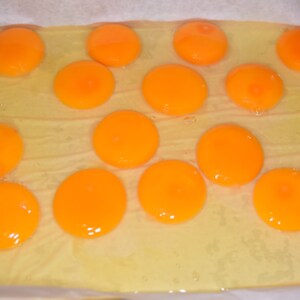 May include: A close-up of a baking sheet with 14 bright orange egg yolks. The yolks are arranged in a pattern on a white parchment paper-lined baking sheet.