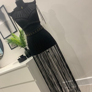 Op de afbeelding: Een zwarte macramé top en rok set met een franje zoom. De top heeft een halterhalslijn en de rok is lang.