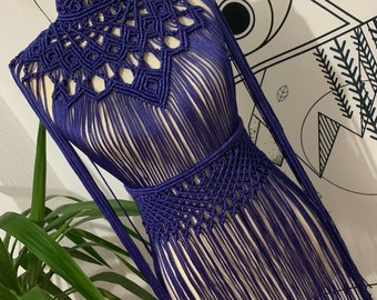May include: A long, navy blue crocheted top with a high neck and fringe detailing. The top is made with a macrame stitch and has a geometric pattern.