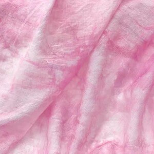 May include: A soft, pink fabric with a tie-dye pattern. The fabric is wrinkled and has a light, airy feel.