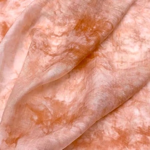 May include: A close-up of a soft, peach-colored fabric with a tie-dye pattern in shades of orange and white.