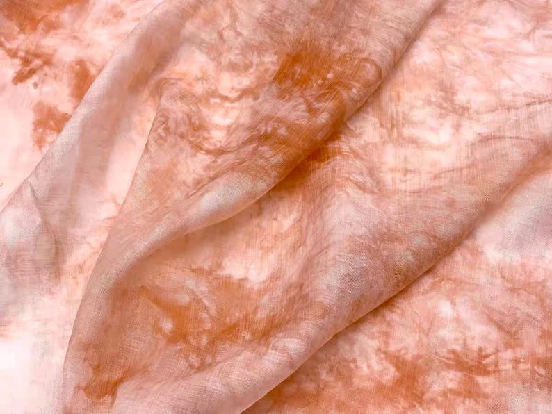 May include: A close-up of a soft, peach-colored fabric with a tie-dye pattern in shades of orange and white.