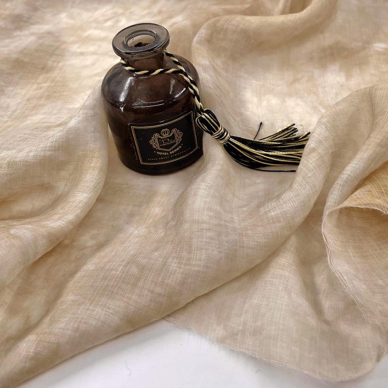May include: A light brown linen scarf with a brown glass bottle with a black and white tassel.