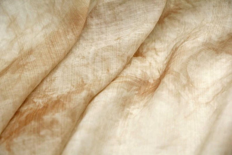 May include: A close-up of a light brown fabric with a subtle, faded pattern. The fabric is soft and has a slightly textured surface.