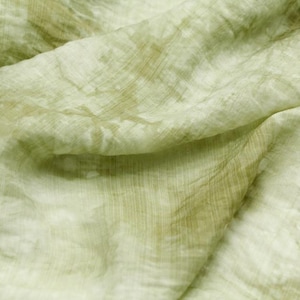 May include: A light green fabric with a subtle, faded pattern. The fabric is soft and has a slightly wrinkled texture.