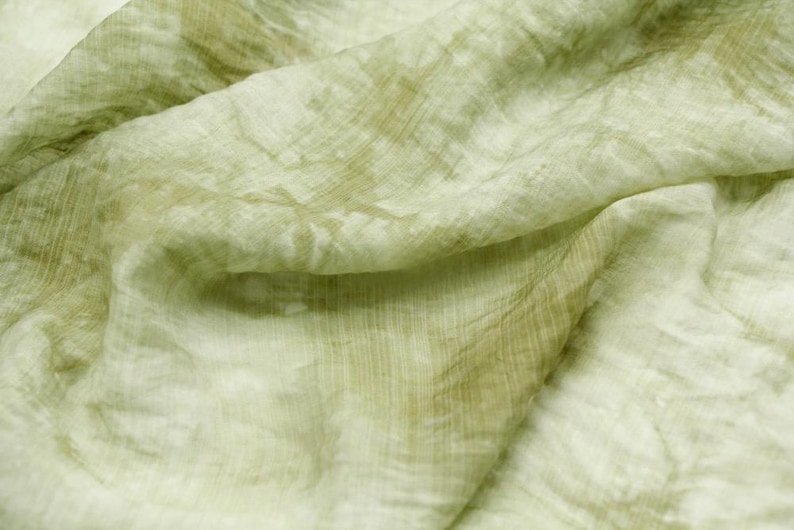 May include: A light green fabric with a subtle, faded pattern. The fabric is soft and has a slightly wrinkled texture.