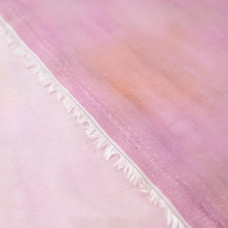 Op de afbeelding: Close-up van stof met een aquareleffect. De stof gaat over van lichtroze naar een diepere paarse tint, met een diagonale naad. De randen van de stof zijn gerafeld.
