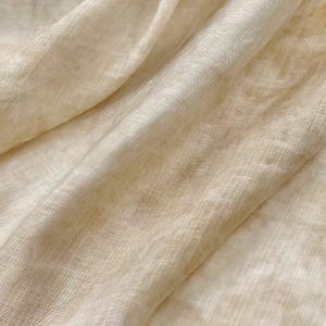 May include: A close-up of a light beige sheer fabric with a subtle woven texture. The fabric is soft and drapes beautifully.