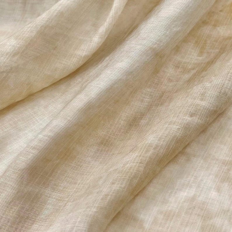 May include: A close-up of a light beige sheer fabric with a subtle woven texture. The fabric is soft and drapes beautifully.