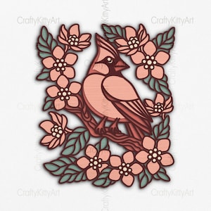 Puede incluir: Una obra de arte de madera en capas que representa un cardenal posado en una rama rodeado de flores y hojas estilizadas. El pájaro y las flores son en tonos de rosa y melocotón, con hojas verdes. La obra de arte está sobre un fondo blanco.