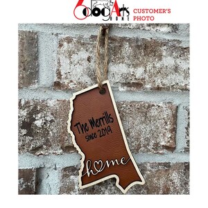 May include: A brown leather and wood state-shaped ornament with the text "The Merrlls since 2019" and "home" with a heart in the word.