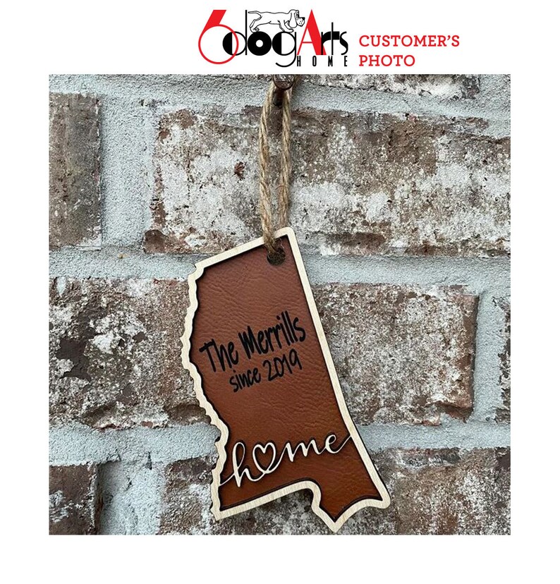 May include: A brown leather and wood state-shaped ornament with the text "The Merrlls since 2019" and "home" with a heart in the word.