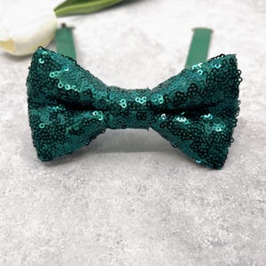 Puede incluir: Una pajarita de lentejuelas color teal. La pajarita está hecha de pequeñas lentejuelas brillantes y tiene una forma de lazo clásica. La correa ajustable para el cuello es de color teal a juego. Es un accesorio formal.