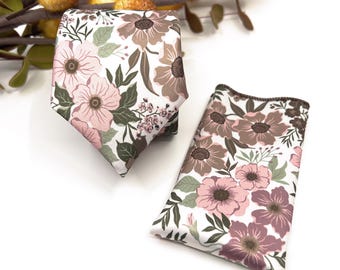 May include: A necktie and a matching pocket square featuring a floral pattern with light pink, dusty rose, and muted green leaves on a white background. The fabric has a smooth finish, and the items are displayed together as a coordinated set.