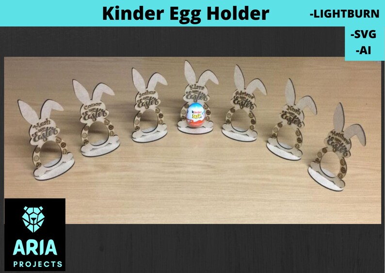 May include: Six wooden bunny-shaped holders for Kinder Eggs. Each holder has the text "Happy Easter" on it. One holder has a Kinder Egg inside.