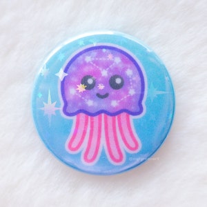 May include: A circular badge featuring a cartoon jellyfish. The jellyfish has a purple head with a constellation design and pink tentacles. The badge has a light blue background with star accents.