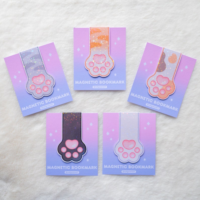 May include: Five different cat paw-shaped magnetic bookmarks with glitter accents. Each bookmark features a different cat paw print design with a pink, purple, and blue gradient background. The text "MAGNETIC BOOKMARK" is printed on each bookmark.